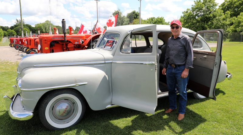 A man poses in front of a classic car.