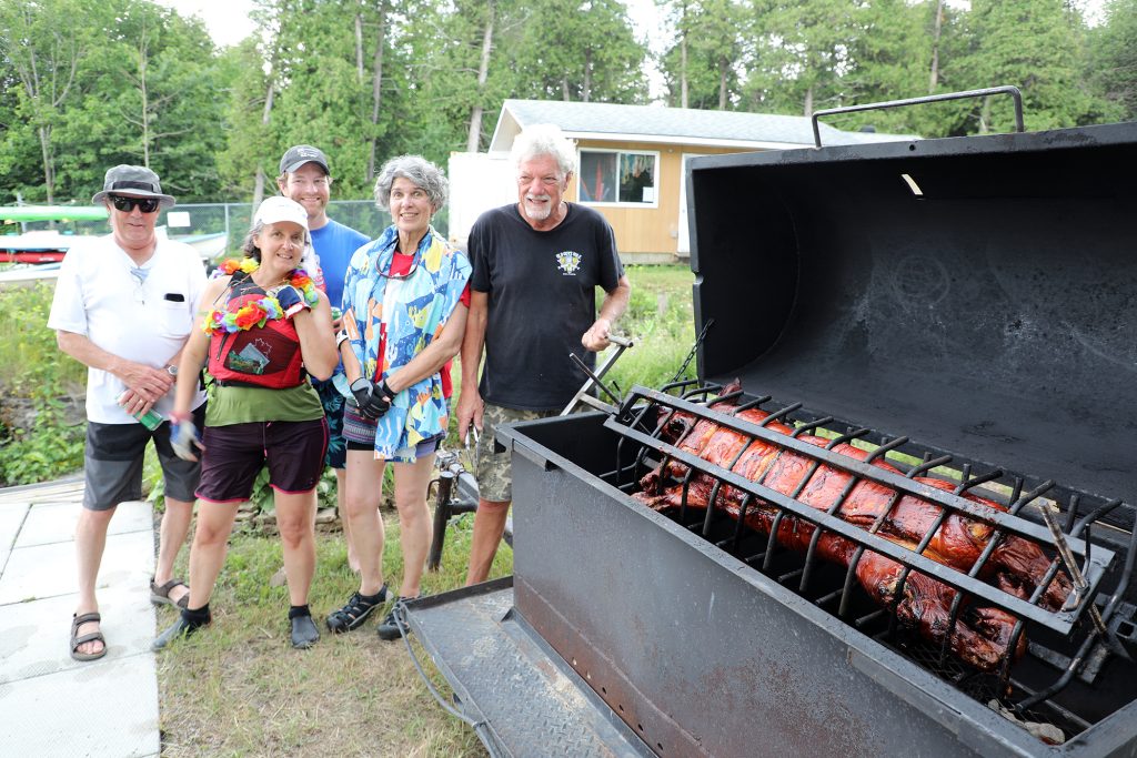 People pose beside a roasting pig.