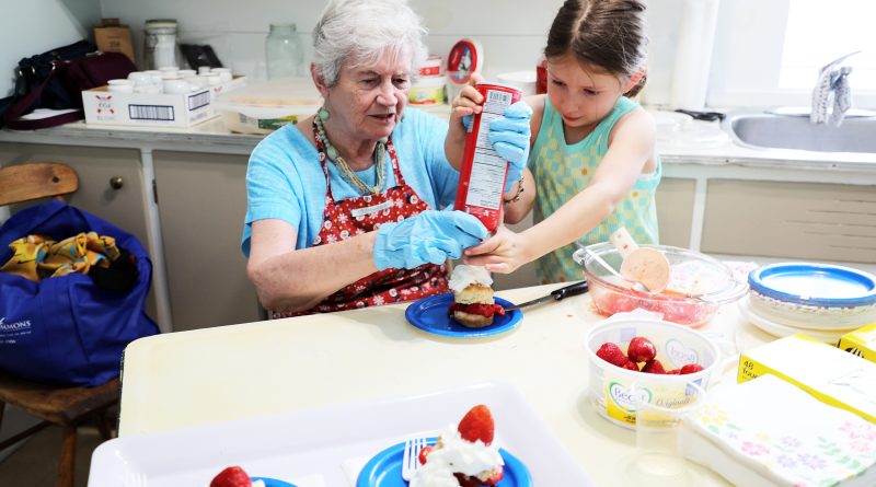 Two people prepare a strawberry shortcake.