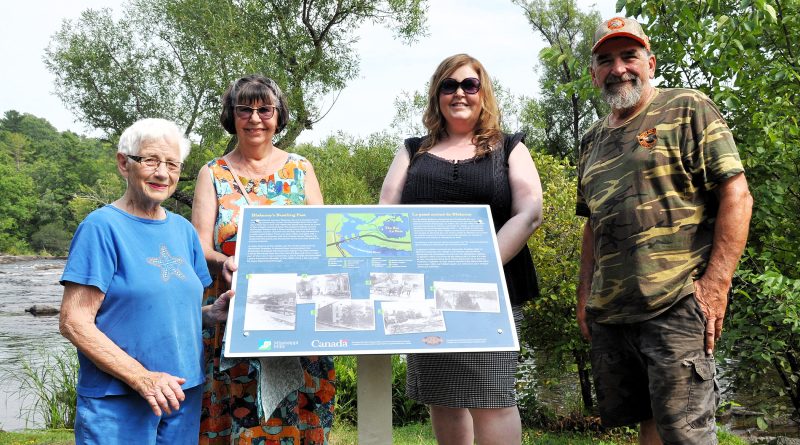 Four people pose by a plaque.