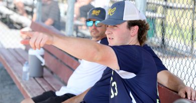 A baseball player talks to coaches on the bench.