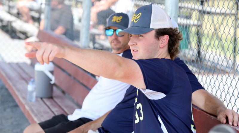A baseball player talks to coaches on the bench.