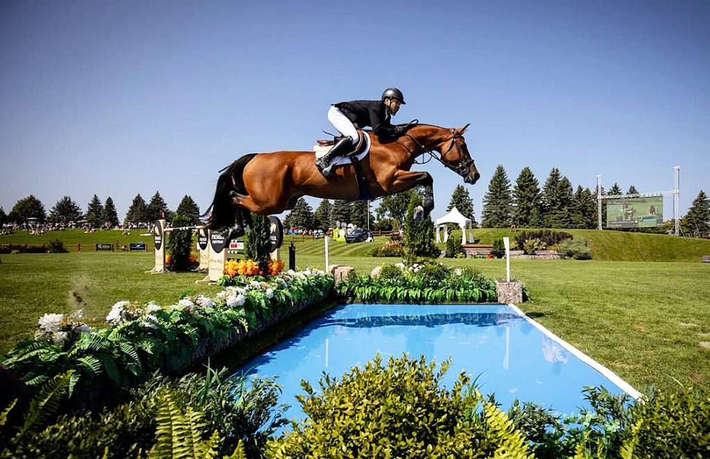 A horse and rider jump over a water jump.