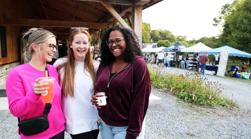 Three women pose in front of a barn.