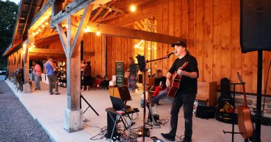 A man plays music outside a barn.