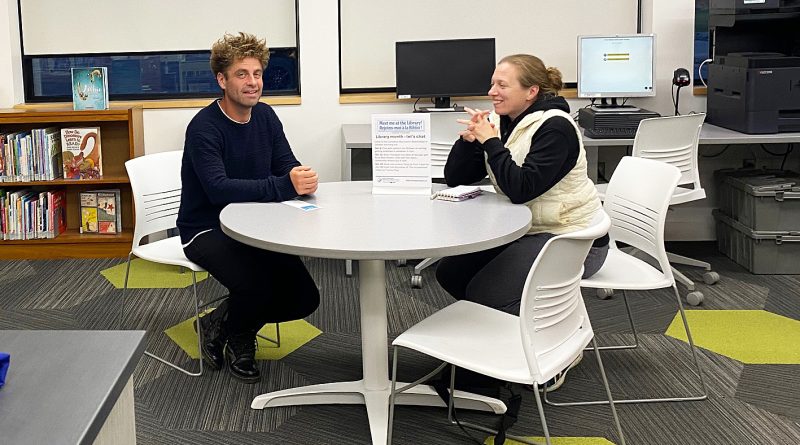 Two people pose in a library.