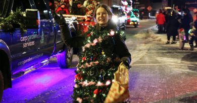 A woman dressed as a Christmas tree waves.