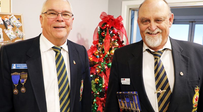 Two people pose in front of a Christmas tree.