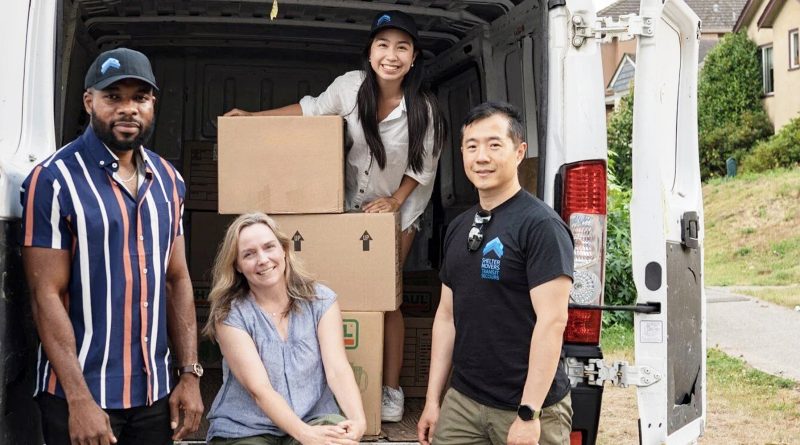 A group poses for a photo in front of a moving van.