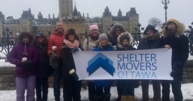 A group of people pose in front of the Parliament Buildings.