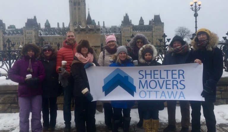 A group of people pose in front of the Parliament Buildings.