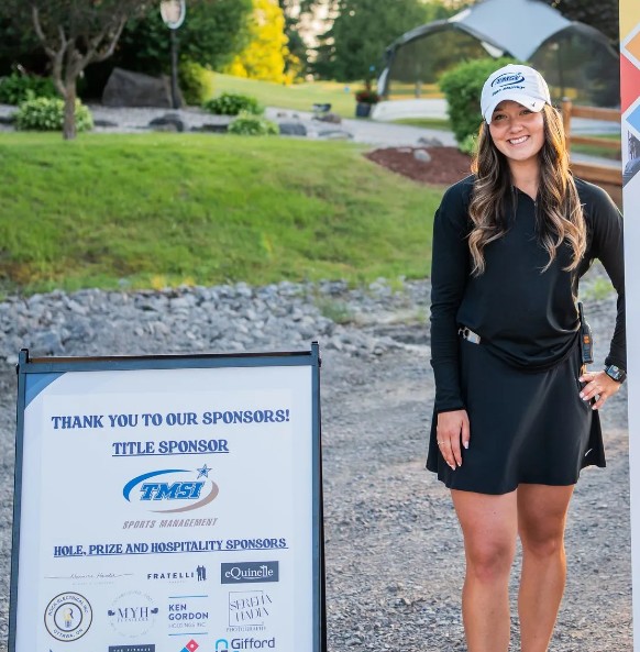 A woman stands next to a sign.