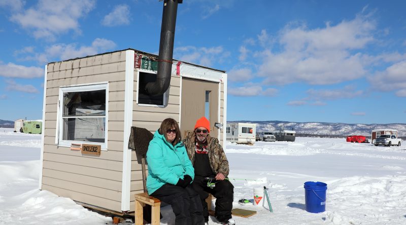 Two people pose outside of an ice shack.