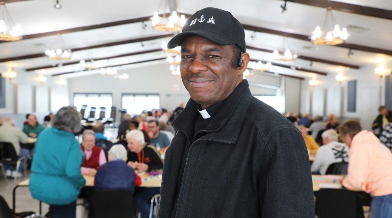 A priest poses for a photo in a busy hall.