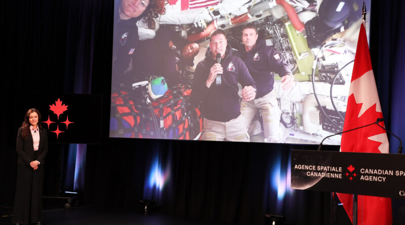 A man on a video screen transmitted from space, answers questions.