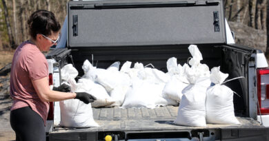 A woman loads a truck with sandbags.
