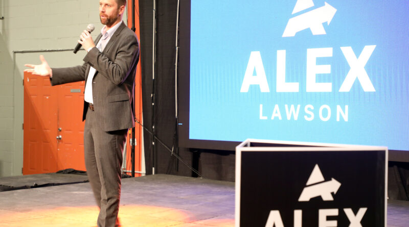 A photo of a person speaking on a stage.