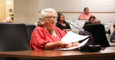 A woman speaks at a desk.