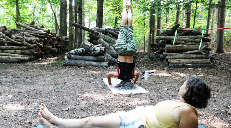 A woman does a headstand in the forest.
